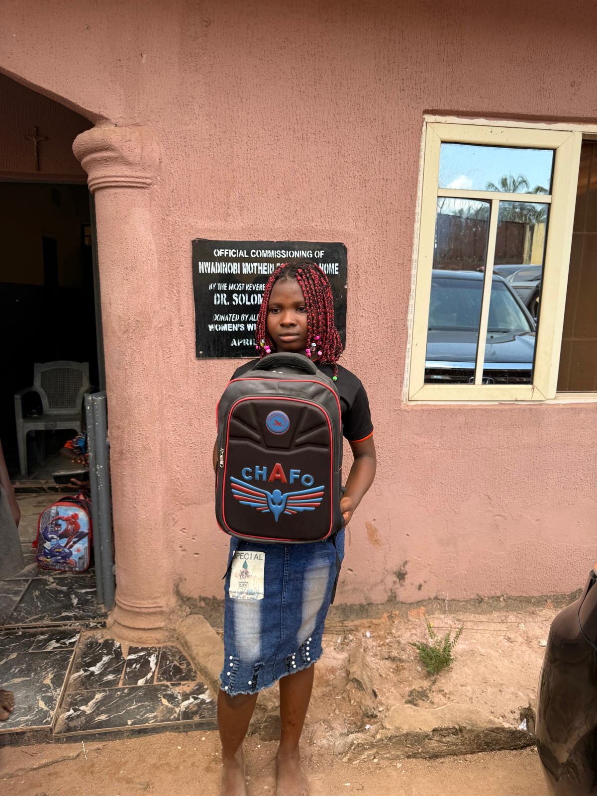 A girl holding a backpack outside the orphanage.
