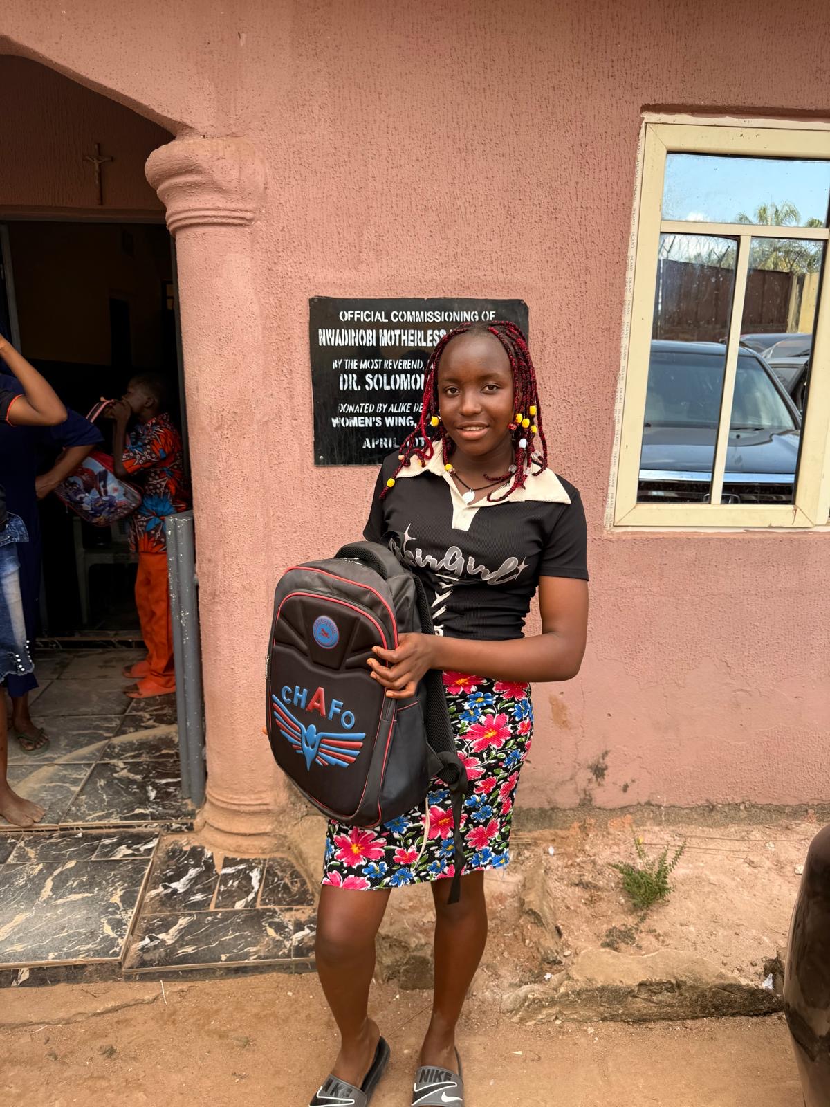 A girl holding a backpack outside the orphanage.