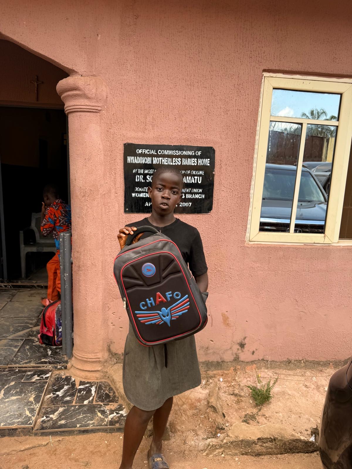 A child holding a backpack outside the orphanage.