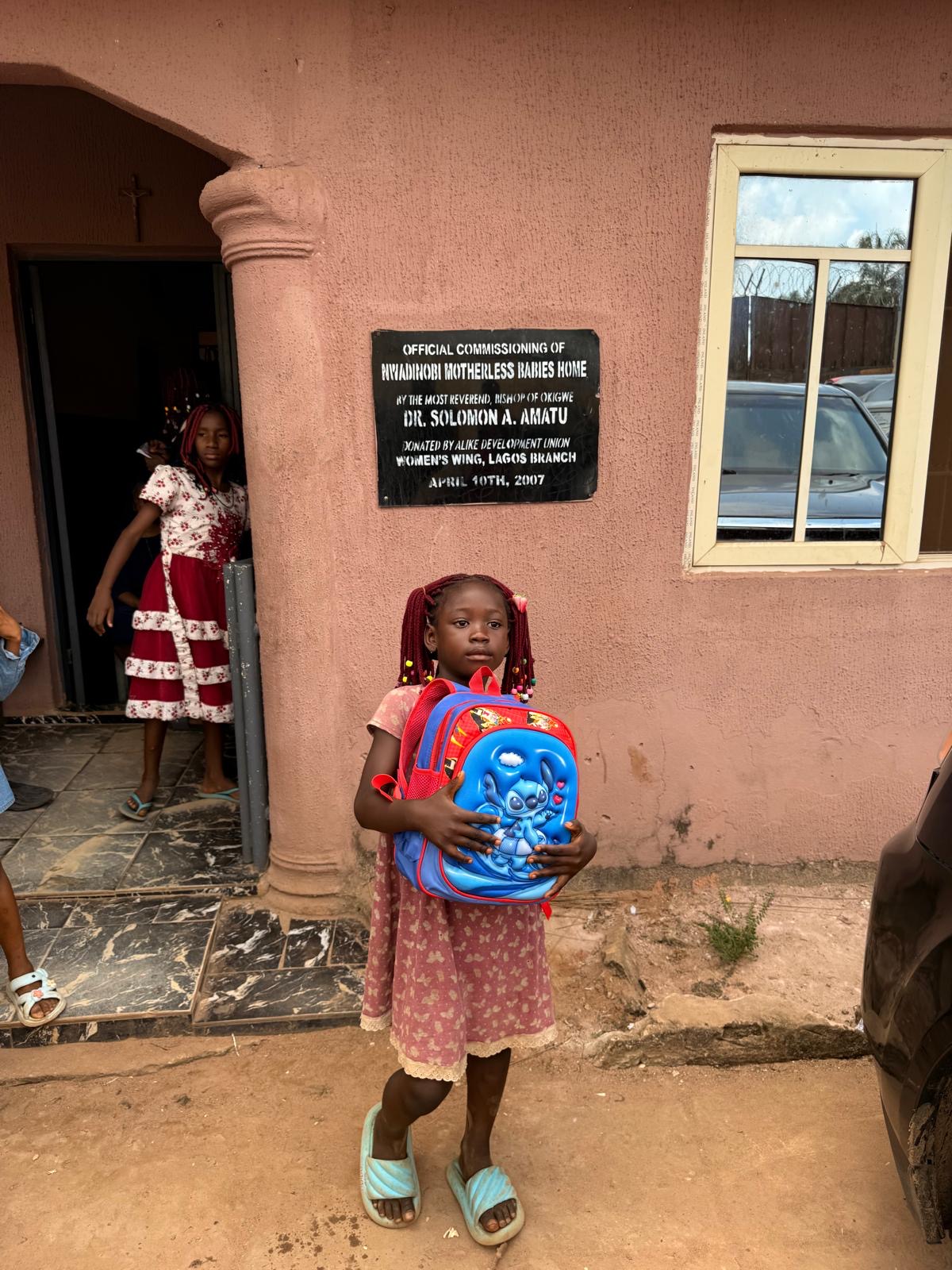 A young child holding a red and blue donated backpack